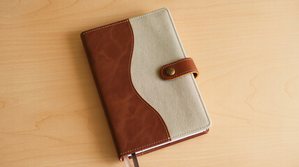 A two-tone brown and beige notebook with a button closure lying on a light wooden table.