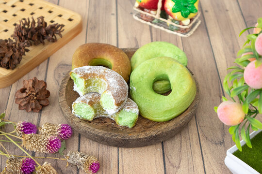 Green pandan donuts, known as donat pandan, served on a wooden plate. Their vibrant color comes from pandan leaf extract, a natural food coloring widely used in Indonesian cuisine.