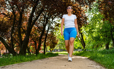 Beautiful middle-aged woman walking in city park on summer day. Front view	