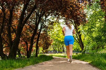 Beautiful middle-aged woman running on jogging track in city park on summer day. Back view	