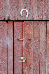 Weathered wooden planks create a rustic barn door, topped by a luck-bringing horseshoe. A sturdy padlock secures the door, hinting at hidden treasures within the tranquil countryside.