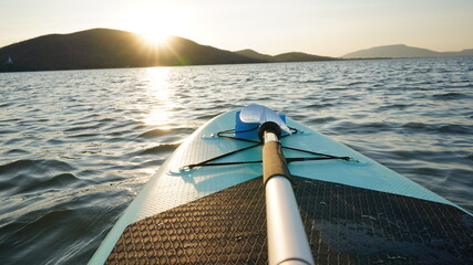 Blue turquoise SUP board in wavy open water. Stand Up Paddle board activity has water sport in the dam during hill in twilight sun. Rowing boat in nature.