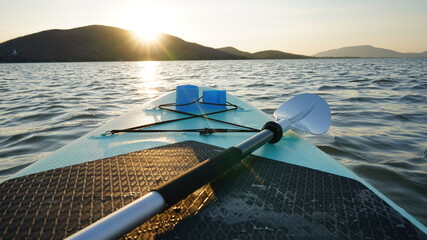 Blue turquoise SUP board in wavy open water. Stand Up Paddle board activity has water sport in the dam during hill in twilight sun. Rowing boat in nature.