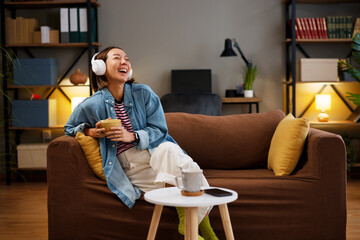 Woman enjoying music and laughing while sitting on a comfortable sofa at home