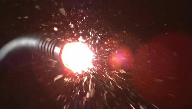 Close up of welding torch in action with bright sparks against dark