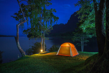 A tent glowing at night in a forest campsite surrounded by trees and nature during a peaceful outdoor camping adventure