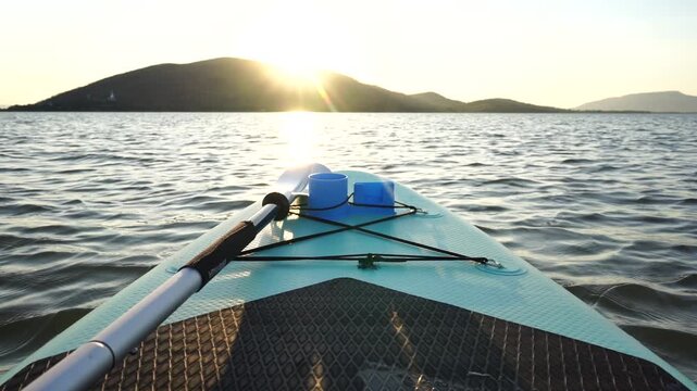 Blue turquoise SUP board in wavy open water. Stand Up Paddle board activity has water sport in the dam during hill in twilight sun. Rowing boat in nature.