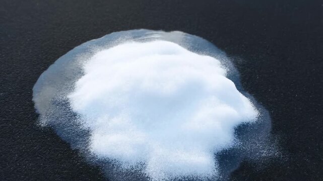 Timelapse of a melting ice pile revealing texture on dark surface