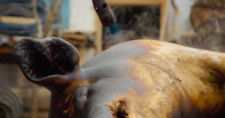 Professional chef carefully burning pig skin with blowtorch, removing hair during traditional meat preparation process in restaurant kitchen