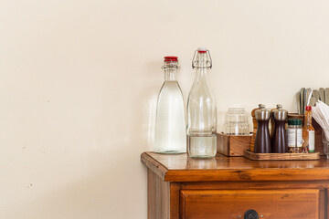 Wooden dresser with two bottles of water and two salt and pepper shakers on top. The bottles of water are clear and the shakers are silver