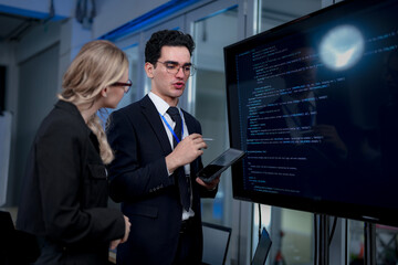 Fototapeta premium A male team leader in a suit uses a stylus to explain a complex project on a large screen, providing one-on-one training to a female colleague in a modern, high-tech office.