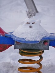 Schneemannn sitzt auf Wackelpferd vom Spielplatz