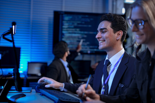 in a coding bootcamp, aspiring software developers take notes during a late-night lecture, studying algorithms and syntax from code displayed on a large screen behind them.