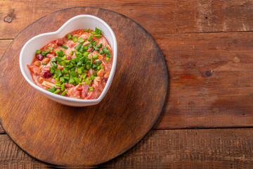 Heart-shaped salad with chicken and beans on a round wooden stand