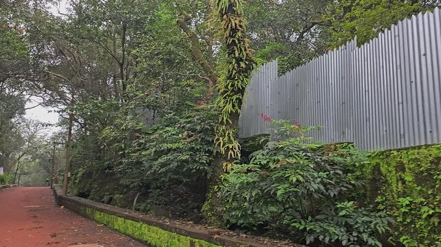Matheran, India &ndash; A metal boundary fence runs along lush greenery, showing subtle human intervention within a protected forest landscape.