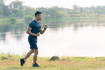 A young Asian man is jogging outdoors in a park in the morning. The concept of exercise for health is depicted.