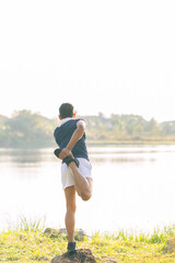 A young man in a T-shirt and shorts is stretching, with the sunlight shining in the background, creating a pre-workout training atmosphere.