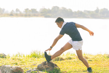A young man in a T-shirt and shorts is stretching, with the sunlight shining in the background, creating a pre-workout training atmosphere.