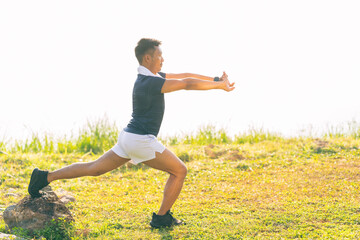 A young man in a T-shirt and shorts is stretching, with the sunlight shining in the background, creating a pre-workout training atmosphere.
