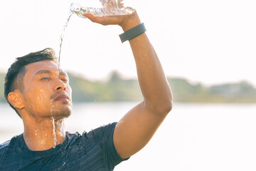 A young Asian man drinks water after exercising in a park during the summer, demonstrating an active and healthy lifestyle.