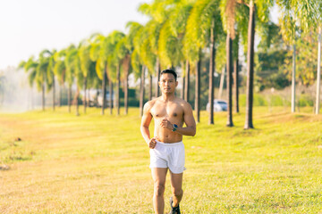 A young Asian man is jogging outdoors in a park in the morning. The concept of exercise for health is depicted.