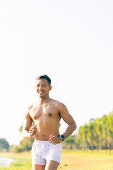 A young Asian man is jogging outdoors in a park in the morning. The concept of exercise for health is depicted.