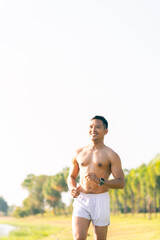 A young Asian man is jogging outdoors in a park in the morning. The concept of exercise for health is depicted.