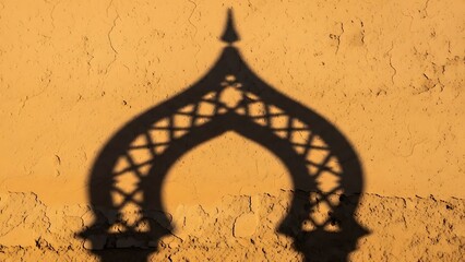 Ornate arch shadow with lattice pattern on textured, cracked orange wall