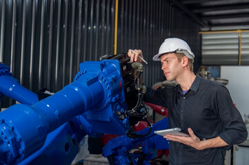 Engineer standing by robotic arm and operating machine in industry factory, technician worker check for repair maintenance electronic operation.