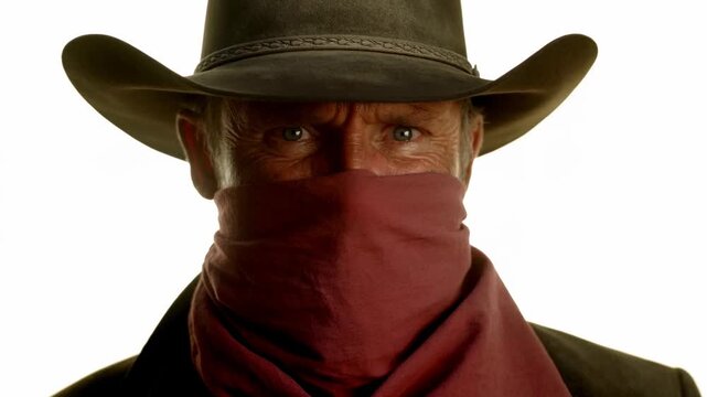 Mysterious cowboy in hat and bandana stares intently into camera with dramatic focus
