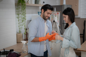 Couple preparing to clean kitchen, helping each other put on gloves.
