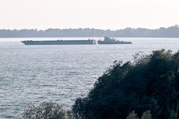 Cargo barge pushed by tugboat on wide river with distant forest shoreline