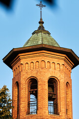 Brick church bell tower with metal cross illuminated by warm evening sunlight
