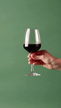 Close Up Hand Holding a Glass of Red Wine Against a Solid Green Background