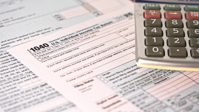 This shows the process of filling out the 1040 US individual income tax return form. A calculator is used to help with the math during tax preparation.