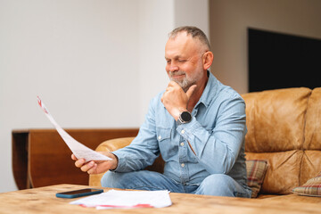 Man reading documents while sitting on sofa in living room during the day