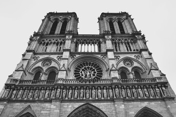フランスのパリにある世界遺産ノートルダム大聖堂の正面ファサードを捉えたモノクロ写真 歴史的なゴシック建築の精密な彫刻や薔薇窓が際立つ白黒のアート 荘厳で神聖な雰囲気を表現したカトリック教会の風景素材