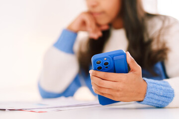 Young person using phone while sitting at desk with papers