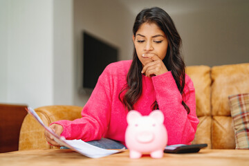 Woman reviewing bills and finances at home with a piggy bank nearby on a couch