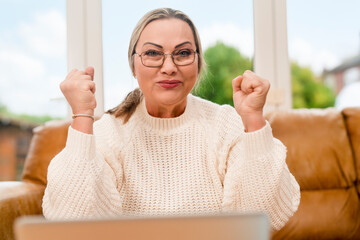 Woman celebrates success while sitting on a couch at home during the day