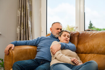 Couple sits on a couch in a living room while embracing each other and sharing a moment