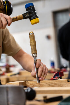 Gros plan sur un artisan utilisant un maillet et un ciseau &agrave; bois pour travailler une pi&egrave;ce de bois en atelier, illustrant la pr&eacute;cision du geste en menuiserie.
