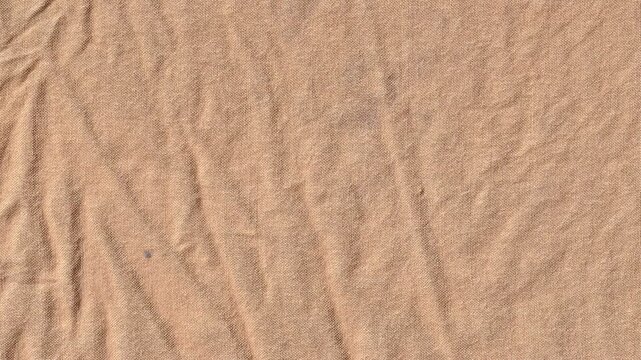 Close up of wrinkled tan cotton fabric texture showing organic creases and folds, perfect for neutral textile backgrounds and minimalist fashion design concepts.
