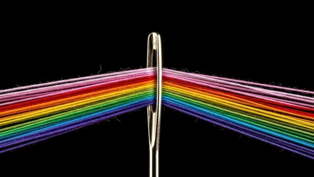 A needle threaded with rainbow-colored threads against black background