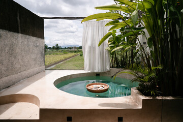 A floating wicker tray with breakfast dishes placed in a small private pool, framed by tropical plants and soft natural light. Calm lifestyle and leisure concept.