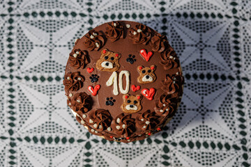 Rich chocolate cake with piped buttercream, teddy bear motifs, hearts, and a bold number ten, displayed on a lace-covered table as a festive celebration centerpiece