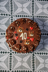 Rich chocolate cake with piped buttercream, teddy bear motifs, hearts, and a bold number ten, displayed on a lace-covered table as a festive celebration centerpiece