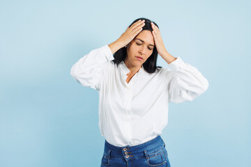 portrait of adult mexican woman with headache pain on blue background in Mexico Latin America, or Latina middle aged brunette female feeling bad