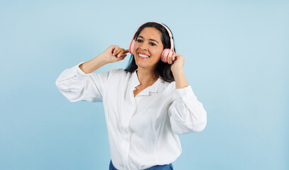 portrait of adult mexican woman listening to music and using headphones on blue background in Mexico Latin America, or Latina middle aged brunette female 