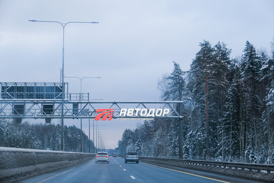 Russia, Saint Petersburg, 11.01.2026 Cars driving on a highway in winter with snow covered trees, displaying an overhead gantry sign. Road trip safety and infrastructure concept.